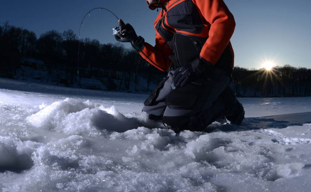 Man ice fishing on a lake in winter