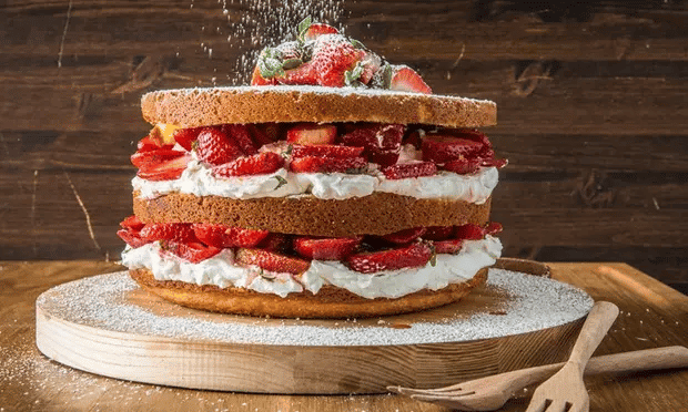 A strawberry shortcake with powdered sugar being sprinkled on top. 